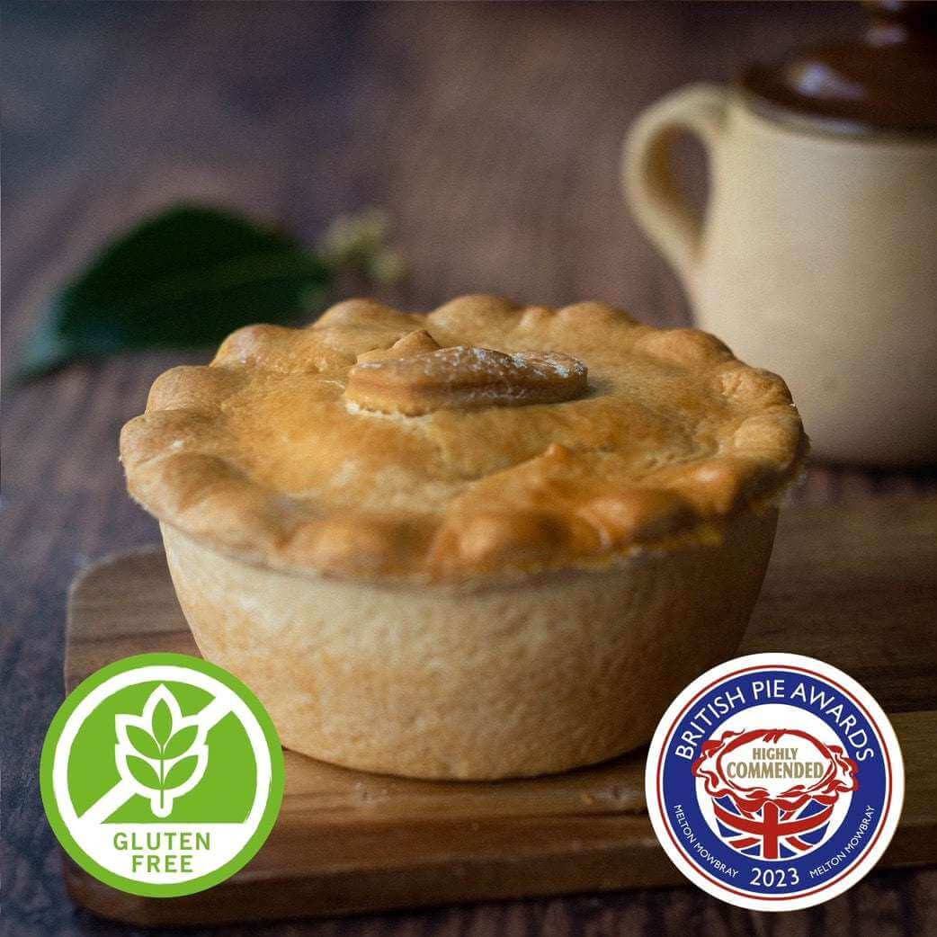 Mud Pies Gluten-Free Steak and Kidney Pie, golden-brown atop a wooden table, with leaf, jug, and award badges in the corners.