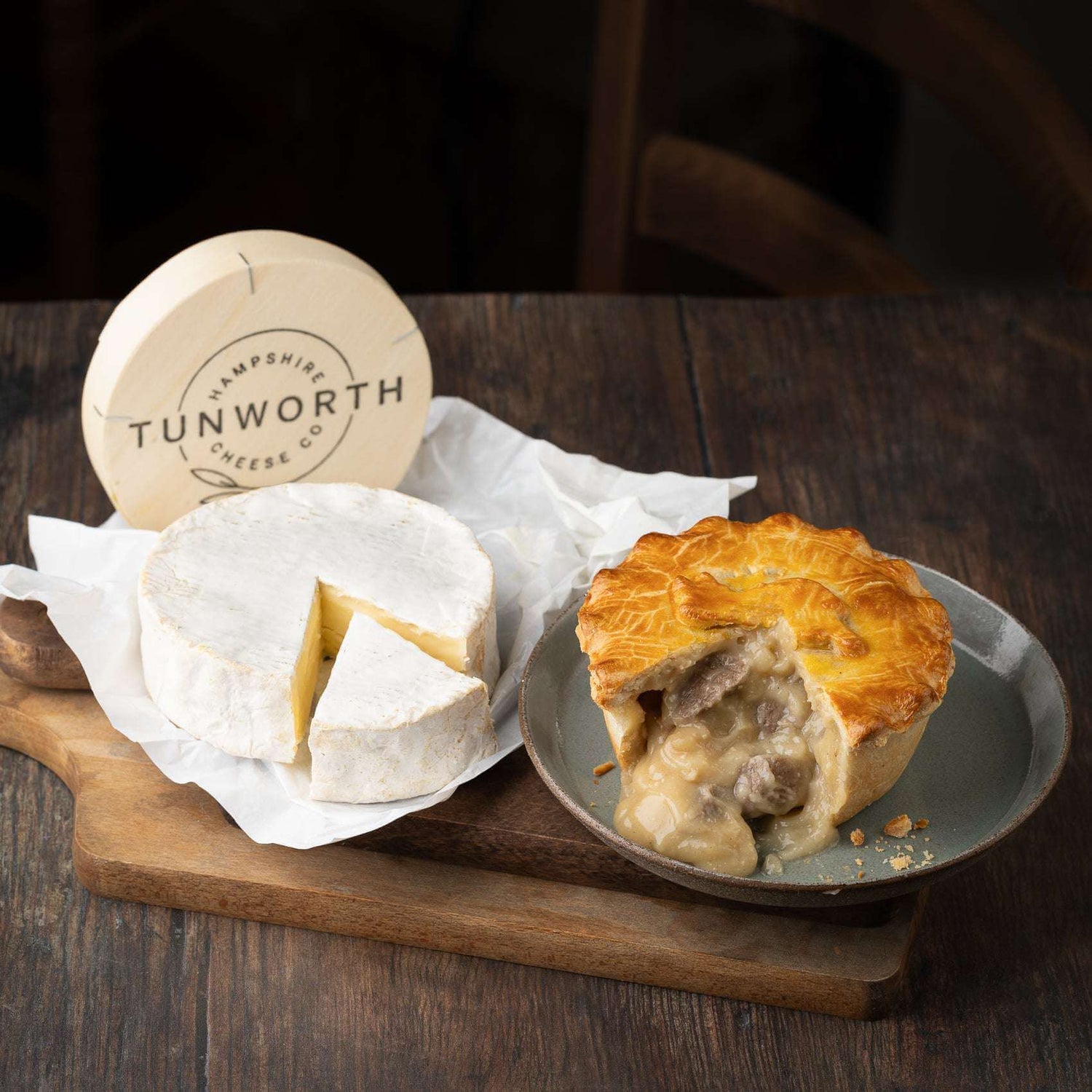 Tunworth cheese wheel on parchment, its soft centre revealed. Beside it, a Mud Pies Steak and Tunworth Cheese Pie with golden pastry.