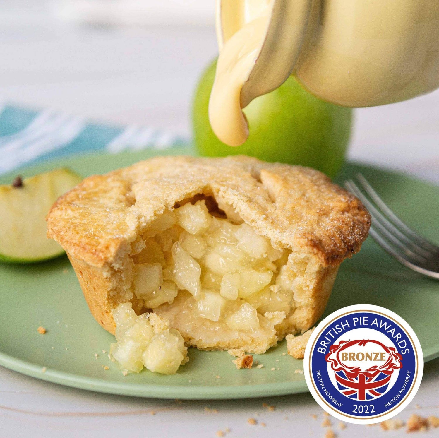 Mud Pies Apple Pie with Cheddar Cheese Crust sits sliced on a green plate, custard pouring over fruity filling; award badge nearby.