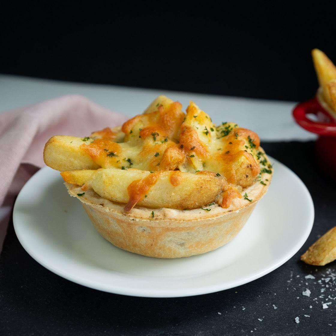 The Mud Pies Chip Top Chicken Royale, a special pie crowned with crispy chips, gooey cheese and herbs, rests on a white plate.