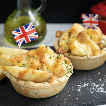 Chip Top Chicken Royale pies by Mud Pies, packed with chips and gooey cheese, crowned by tiny UK flags on salty dark slate.