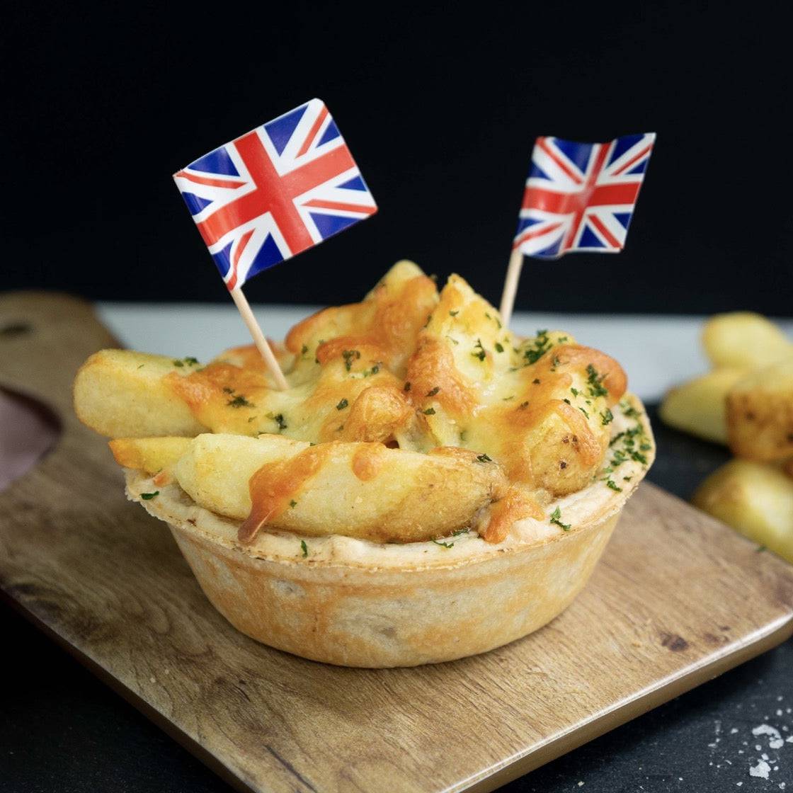 Mud Pies' Chip Top Steak Royale boasts steak and ale pie, chunky chips, melted cheese, herbs, on a wooden board with UK flags.