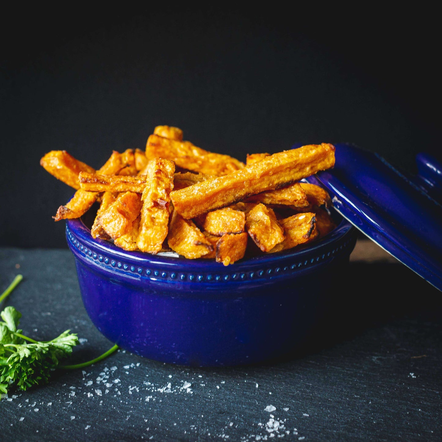 Mud Pies Sweet Potato Fries in a deep blue bowl, golden and crisp, sprinkled with coarse salt and parsley for a vibrant twist.