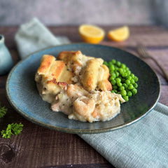 Mud Pies' Luxury Fish Pie with Scottish Salmon and golden pastry sits on blue china, with peas, lemon wedges, and fork nearby.