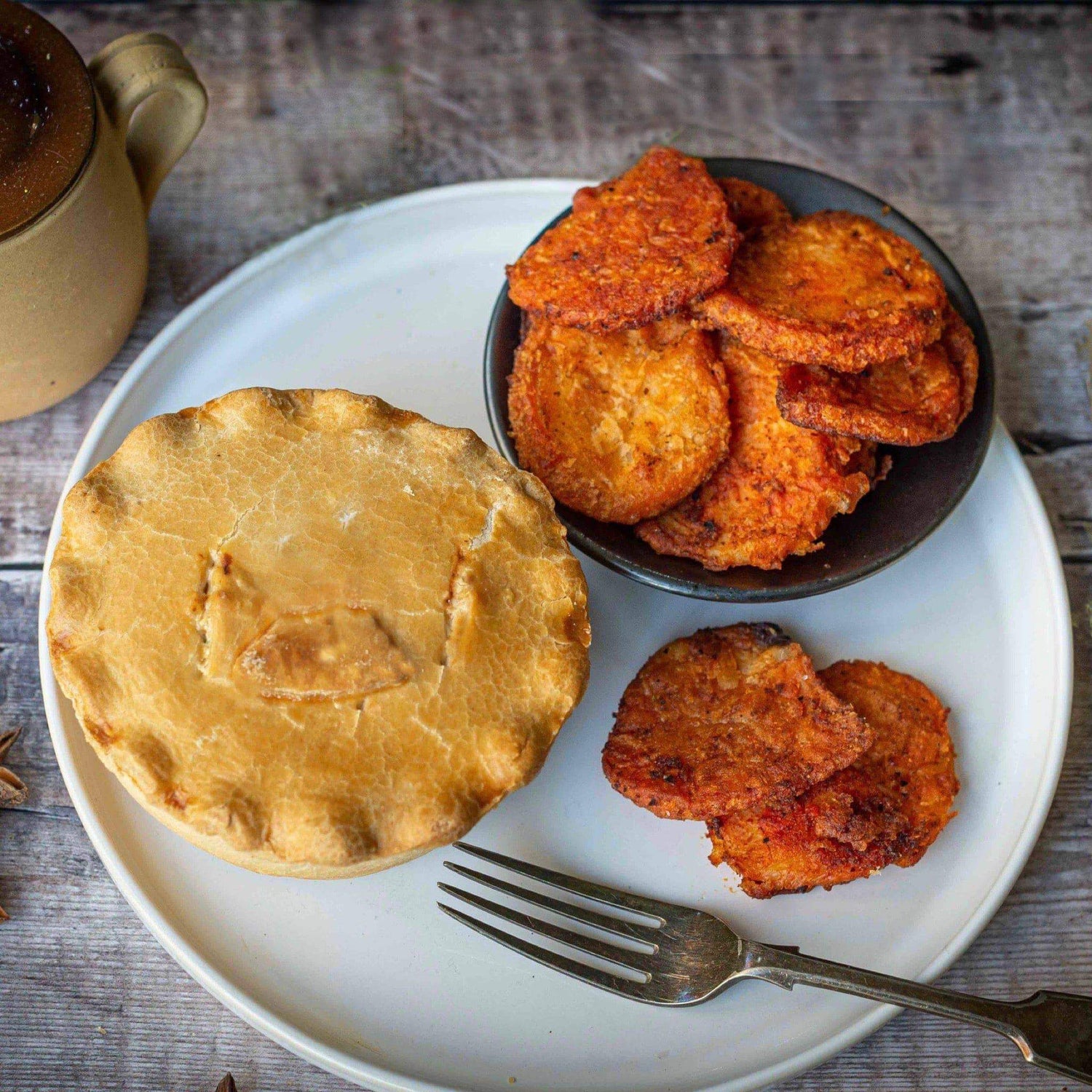 Mud Pies Southern Fried Potatoes sit on a plate with a golden, flaky pie, a fork, extra crispy spuds in a bowl and coffee nearby.